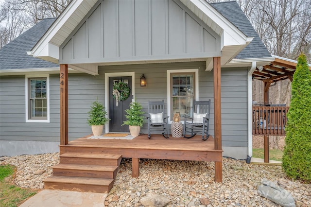 view of exterior entry with board and batten siding, covered porch, and roof with shingles