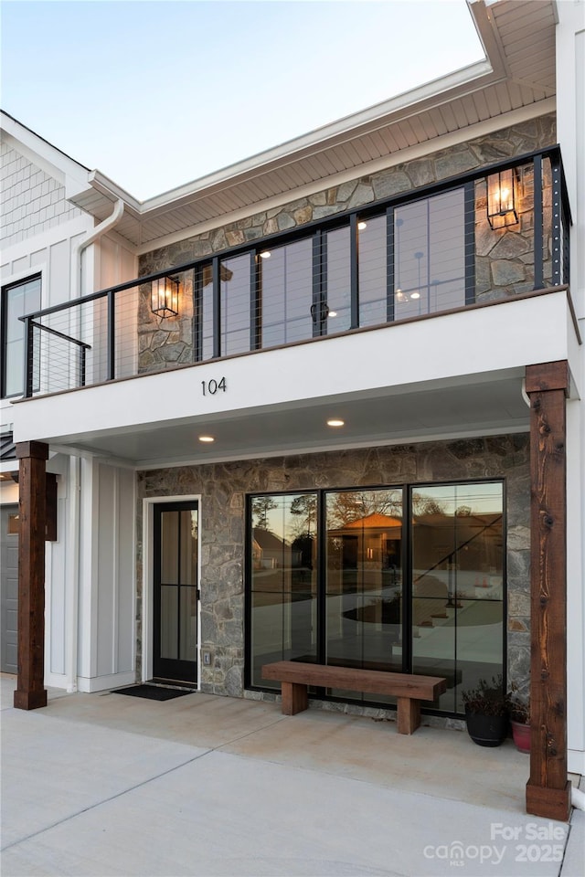 view of exterior entry featuring a balcony, board and batten siding, and stone siding