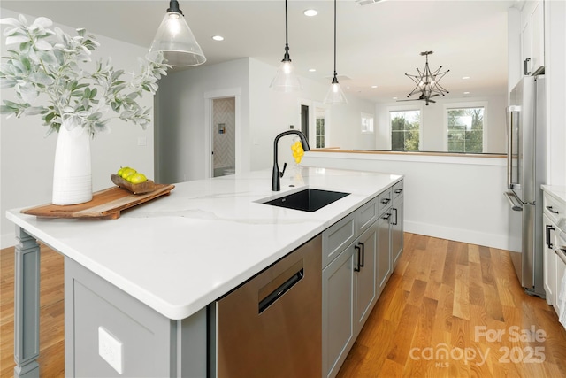 kitchen featuring a sink, gray cabinetry, light wood-style floors, stainless steel appliances, and a kitchen island with sink