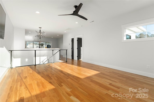 empty room featuring recessed lighting, ceiling fan with notable chandelier, baseboards, and wood finished floors