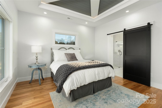 bedroom featuring visible vents, baseboards, a barn door, light wood-style flooring, and a raised ceiling