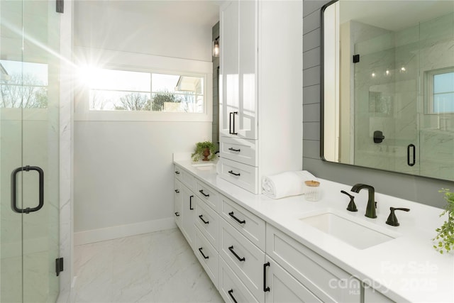 full bath with marble finish floor, a stall shower, a sink, double vanity, and baseboards