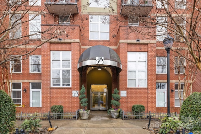 view of exterior entry featuring brick siding and fence