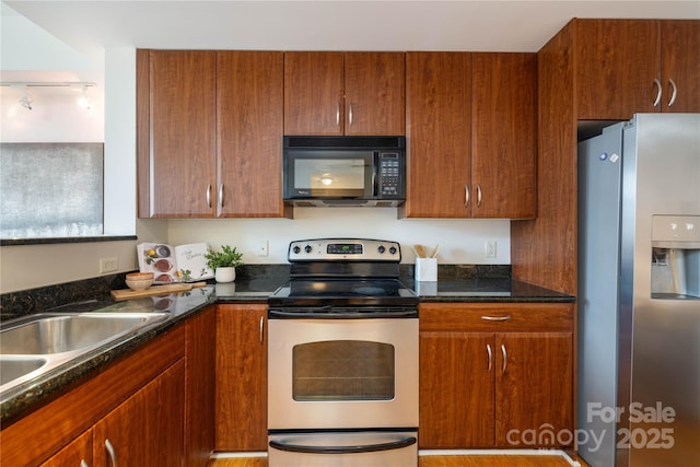 kitchen featuring dark stone countertops, brown cabinetry, appliances with stainless steel finishes, and a sink