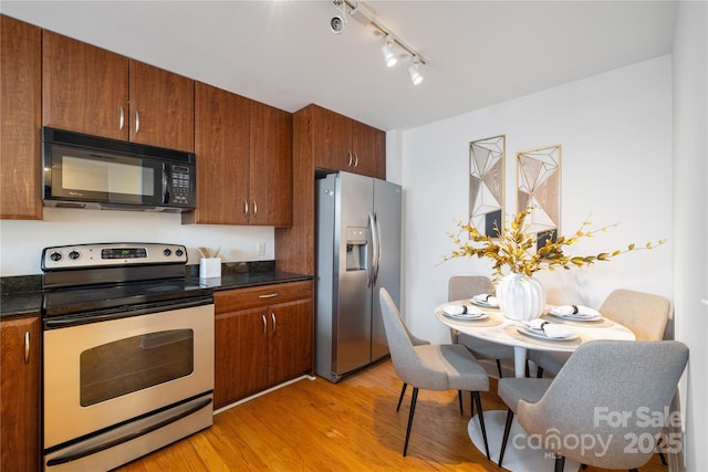 kitchen featuring stainless steel appliances, dark countertops, brown cabinetry, and light wood finished floors