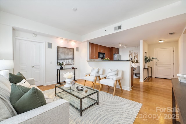 living room with light wood-style floors, visible vents, and baseboards