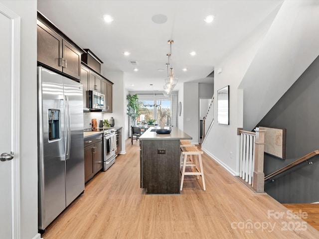 kitchen featuring a center island with sink, a sink, stainless steel appliances, light countertops, and dark brown cabinets