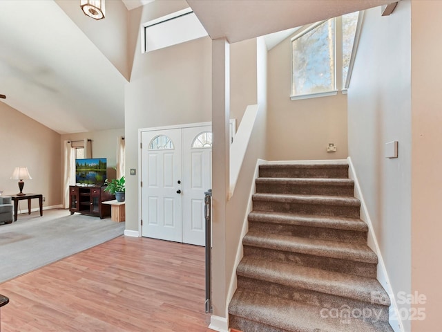 foyer featuring a high ceiling, stairway, wood finished floors, and baseboards