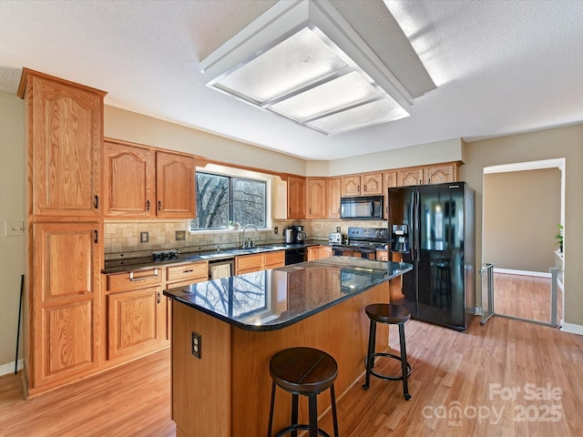 kitchen featuring black appliances, a sink, a kitchen breakfast bar, a center island, and light wood-style floors