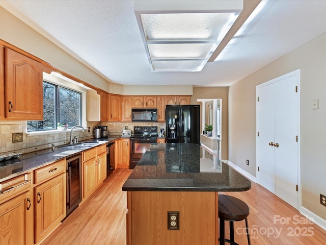 kitchen featuring a kitchen bar, black appliances, beverage cooler, a sink, and a center island