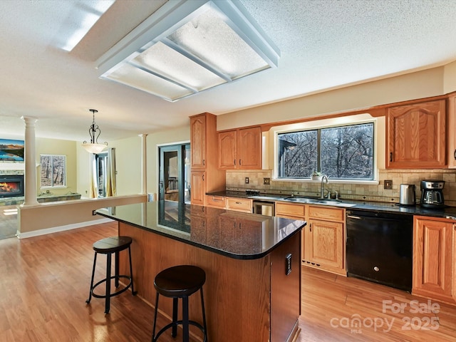 kitchen with a kitchen island, black dishwasher, decorative columns, light wood-style flooring, and a sink