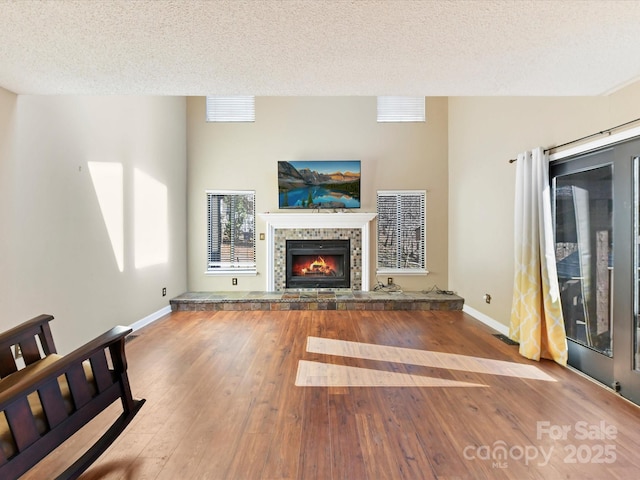 unfurnished living room featuring visible vents, baseboards, a tiled fireplace, hardwood / wood-style floors, and a textured ceiling