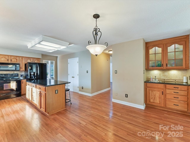 kitchen with dark countertops, a kitchen breakfast bar, black appliances, and light wood-type flooring