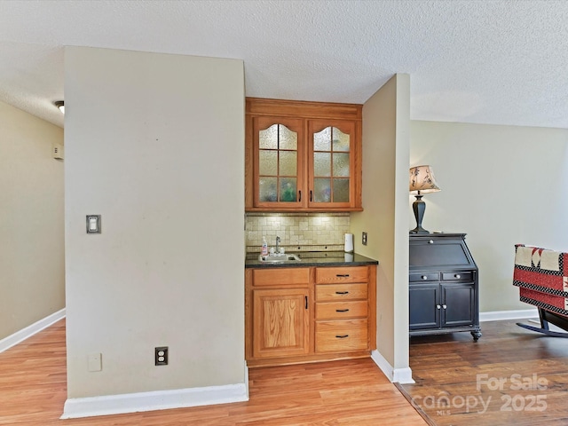 bar featuring tasteful backsplash, light wood-style flooring, and a sink