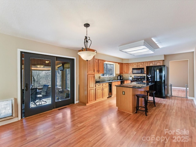 kitchen with a kitchen island, black appliances, light wood-style flooring, and a breakfast bar