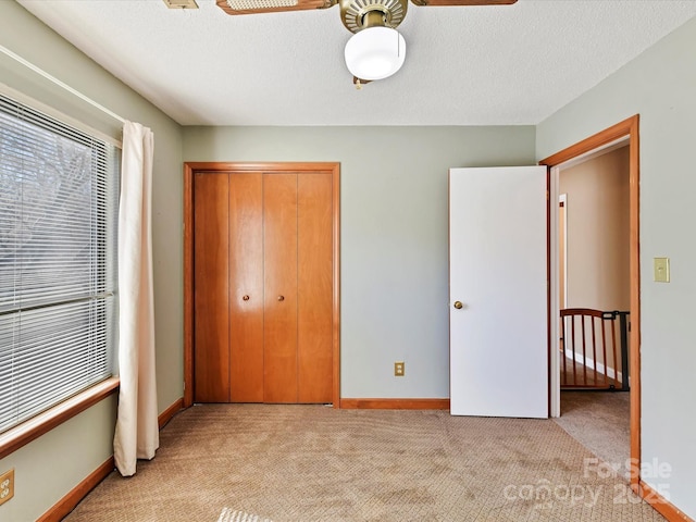 unfurnished bedroom featuring a closet, light carpet, a textured ceiling, and baseboards