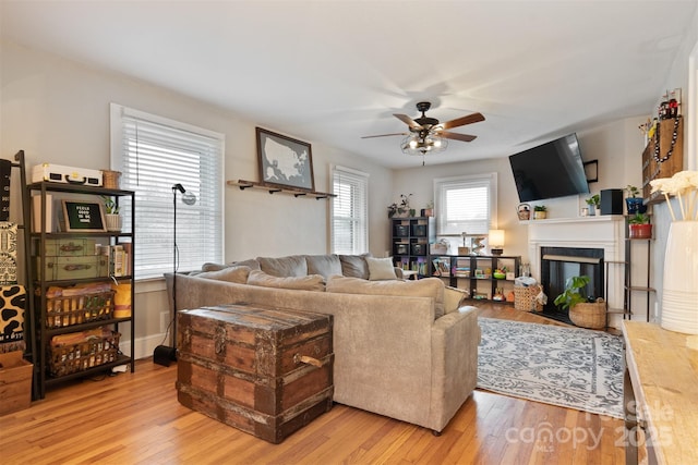 living room featuring light wood finished floors, a glass covered fireplace, and a ceiling fan