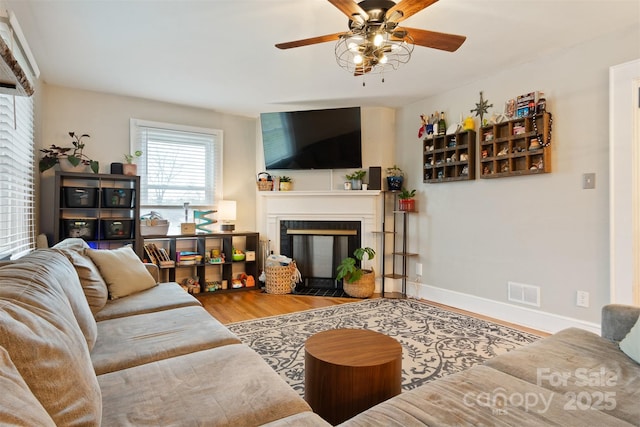 living room featuring visible vents, ceiling fan, baseboards, a fireplace with flush hearth, and wood finished floors