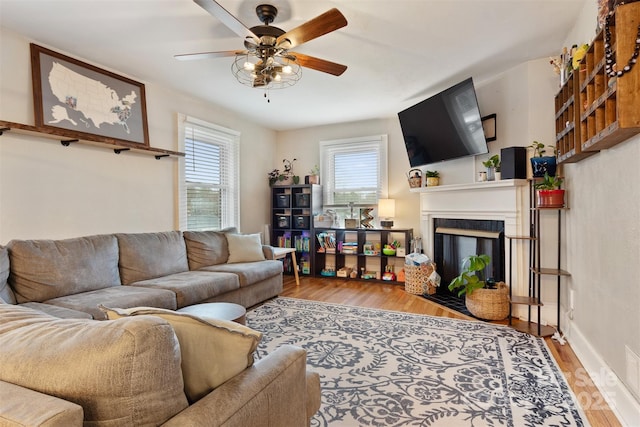 living area featuring a ceiling fan, a fireplace with flush hearth, wood finished floors, and baseboards