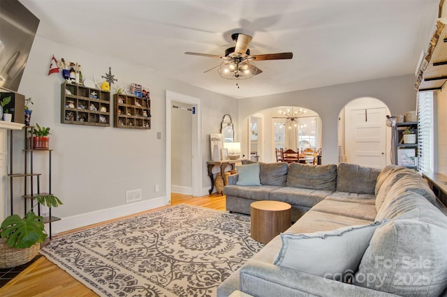 living area with arched walkways, ceiling fan with notable chandelier, baseboards, and wood finished floors