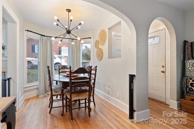 dining room with visible vents, baseboards, light wood-type flooring, an inviting chandelier, and arched walkways