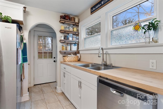 kitchen with wooden counters, arched walkways, white cabinets, stainless steel appliances, and a sink