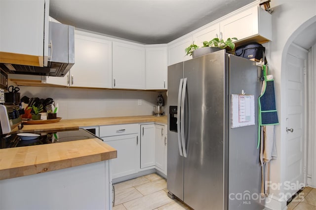 kitchen featuring light tile patterned flooring, arched walkways, white cabinetry, stainless steel fridge, and butcher block counters