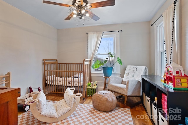 bedroom featuring a nursery area, wood finished floors, and a ceiling fan