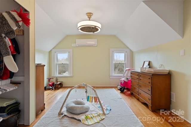 rec room featuring an AC wall unit, light wood-type flooring, and vaulted ceiling