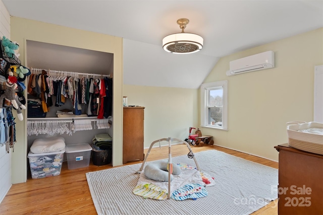 bedroom with a wall unit AC, wood finished floors, a closet, and vaulted ceiling