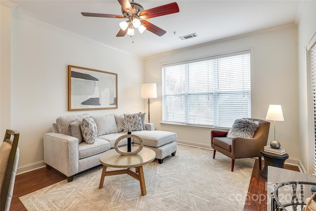 living area featuring visible vents, baseboards, ornamental molding, light wood-style floors, and a ceiling fan