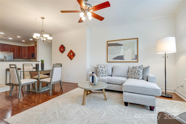 living room featuring light wood-style flooring, ceiling fan with notable chandelier, crown molding, and baseboards