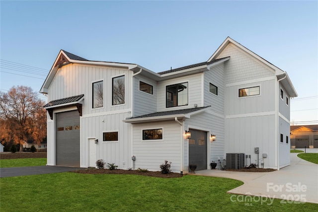 modern inspired farmhouse with a front lawn, driveway, a standing seam roof, board and batten siding, and an attached garage