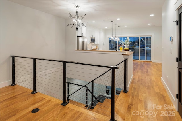 corridor featuring an upstairs landing, light wood-style flooring, recessed lighting, an inviting chandelier, and baseboards