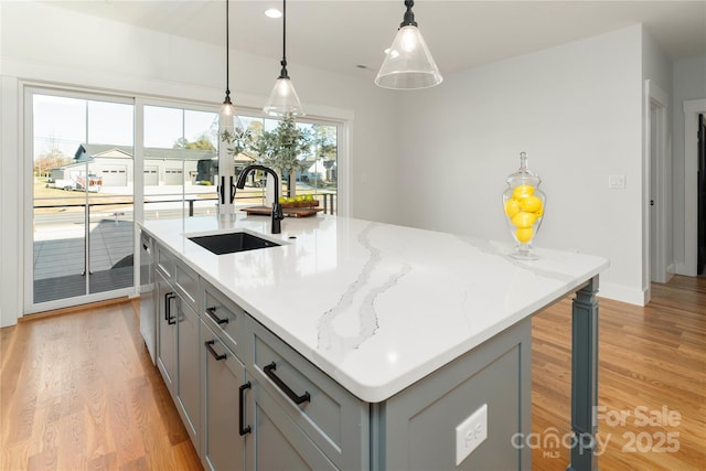 kitchen featuring a center island with sink, light wood-style flooring, gray cabinets, a sink, and decorative light fixtures