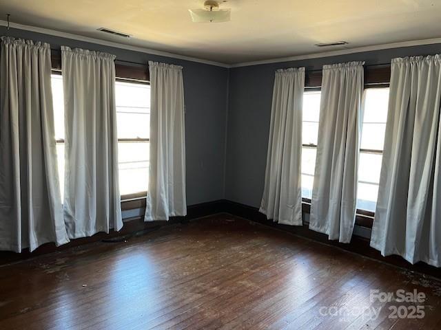 unfurnished room featuring visible vents, dark wood-style flooring, and ornamental molding