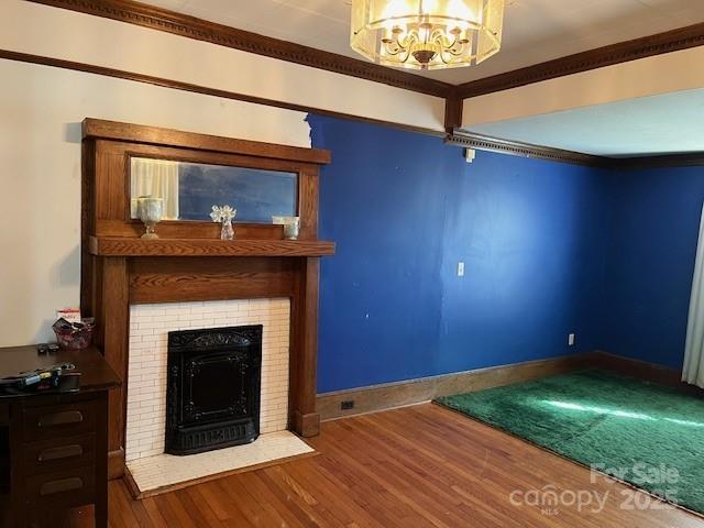 unfurnished living room featuring wood finished floors, an inviting chandelier, a fireplace, crown molding, and baseboards