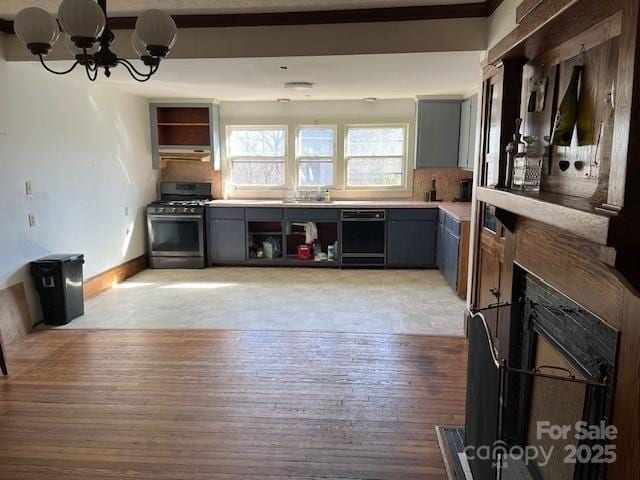 kitchen featuring gray cabinetry, light wood-type flooring, an inviting chandelier, stainless steel gas range, and open shelves