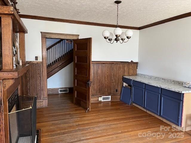 dining area with light wood finished floors, a chandelier, a textured ceiling, and a wainscoted wall