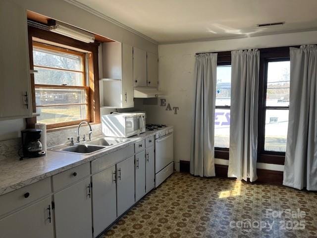 kitchen featuring under cabinet range hood, light countertops, tile patterned floors, white appliances, and a sink