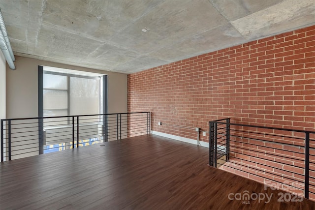 unfurnished room featuring wood finished floors and brick wall