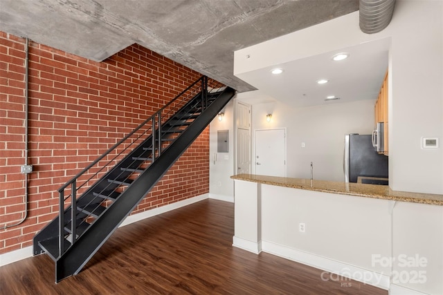 interior space with electric panel, wood finished floors, recessed lighting, brick wall, and baseboards