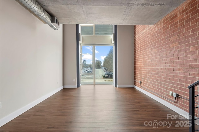 unfurnished living room featuring dark wood finished floors, floor to ceiling windows, baseboards, and brick wall