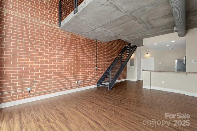 unfurnished living room featuring stairway, wood finished floors, baseboards, and brick wall