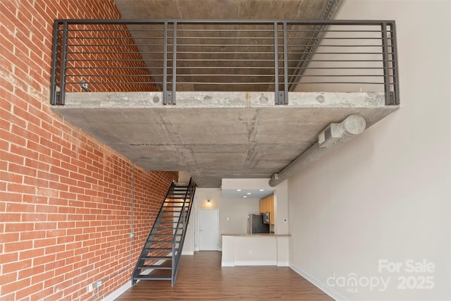 stairway with baseboards, wood finished floors, and brick wall