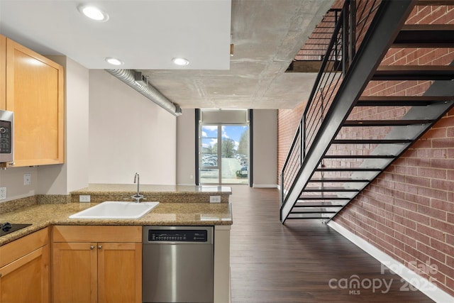 kitchen featuring brick wall, a peninsula, a sink, light brown cabinetry, and stainless steel appliances