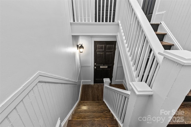 stairway with a wainscoted wall and wood finished floors