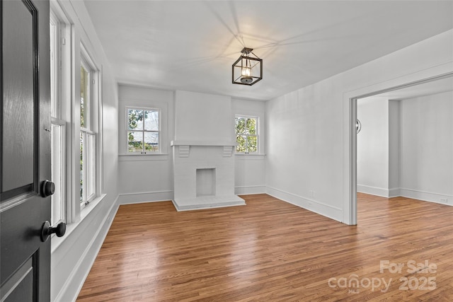 unfurnished living room featuring a brick fireplace, wood finished floors, and baseboards