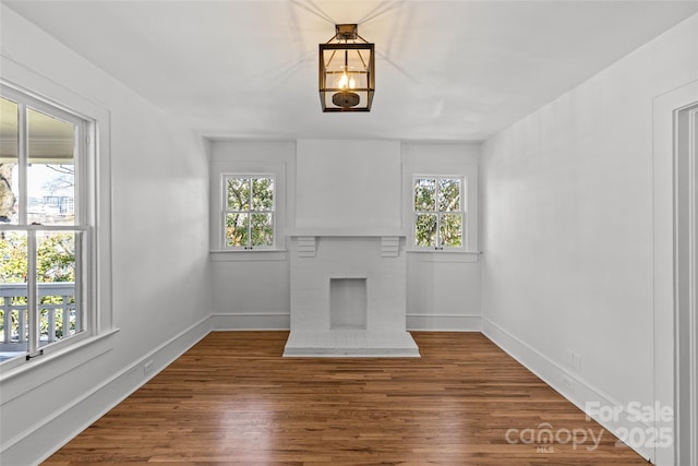 unfurnished living room featuring baseboards, a brick fireplace, and wood finished floors