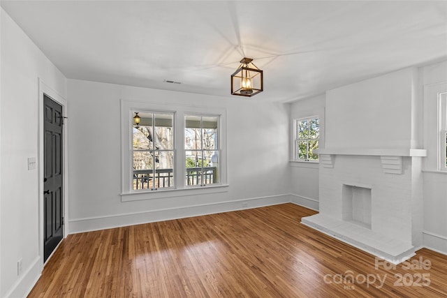 unfurnished living room with a fireplace, wood finished floors, visible vents, and baseboards